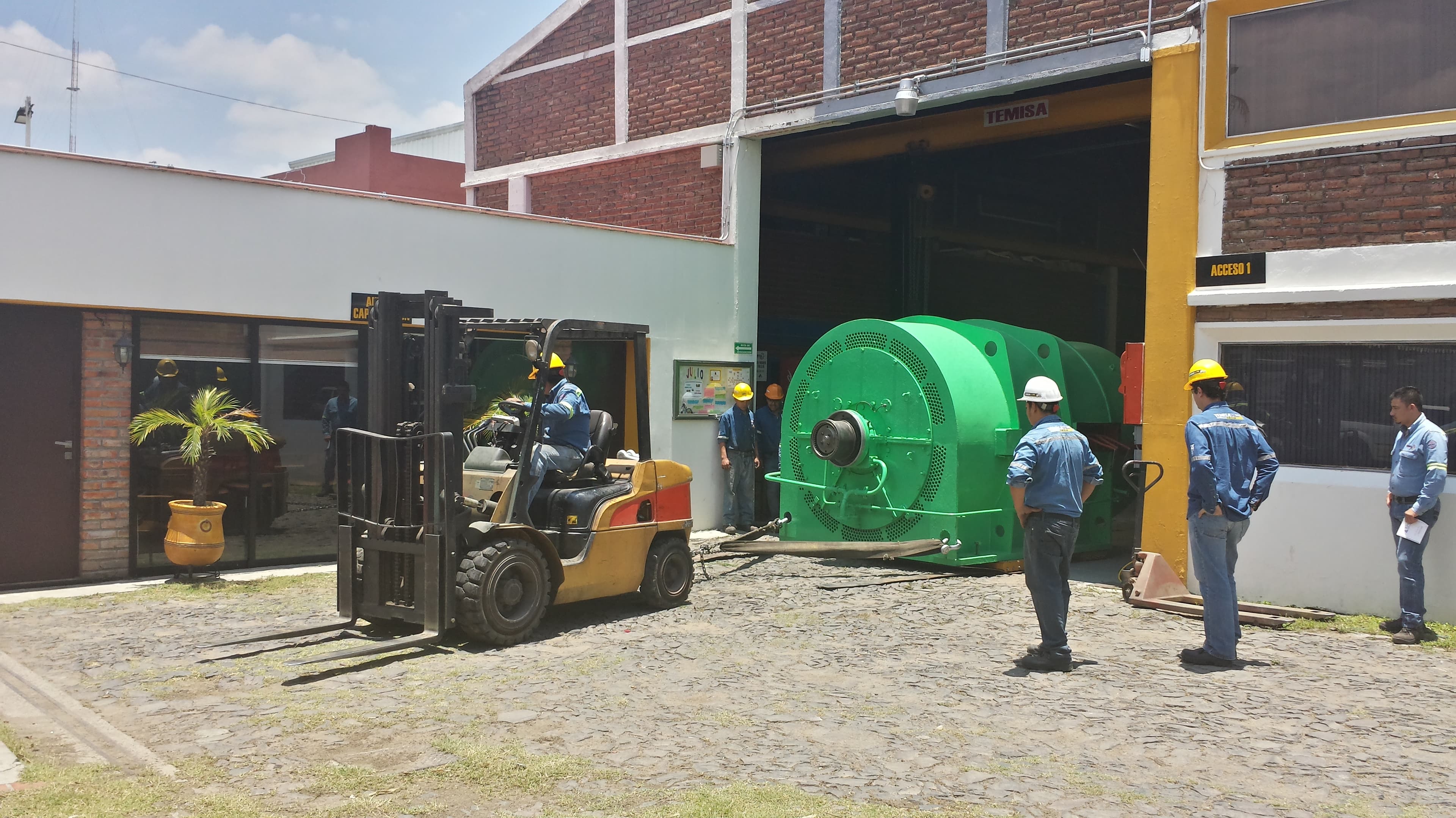 Equipo TEMISA moviendo generador eléctrico industrial verde con montacargas y grúa viajera en el taller moderno