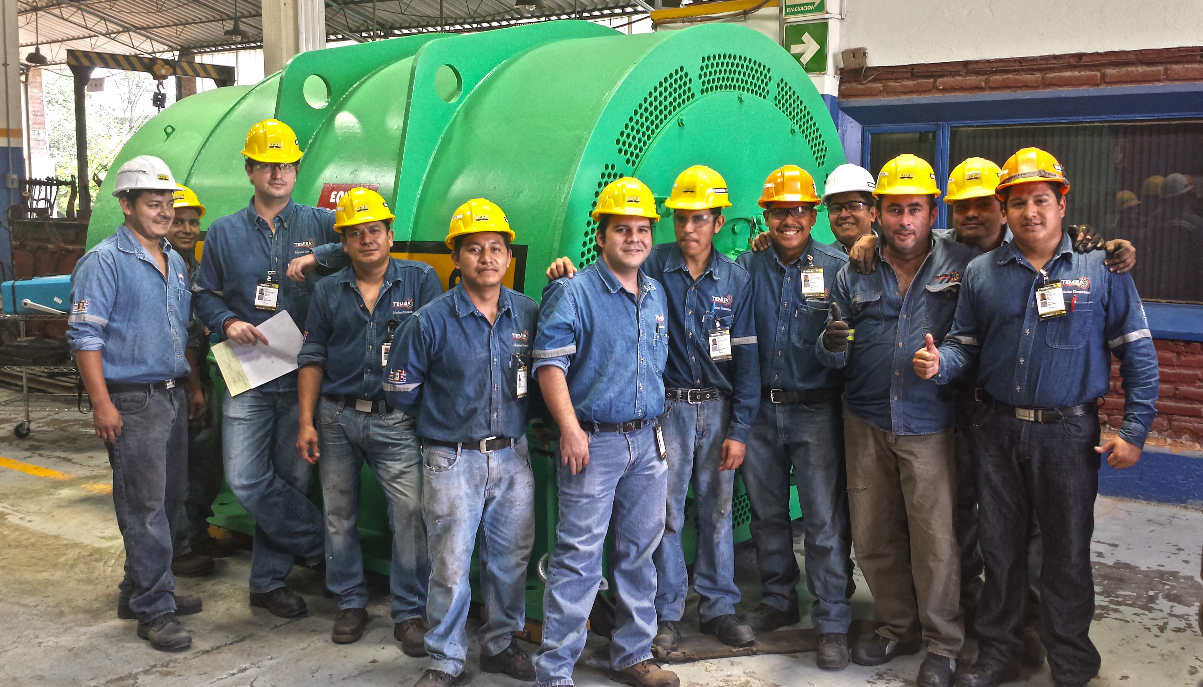 Equipo completo de técnicos TEMISA Power Gen frente a turbogenerador verde en taller Tlajomulco — talento humano del taller