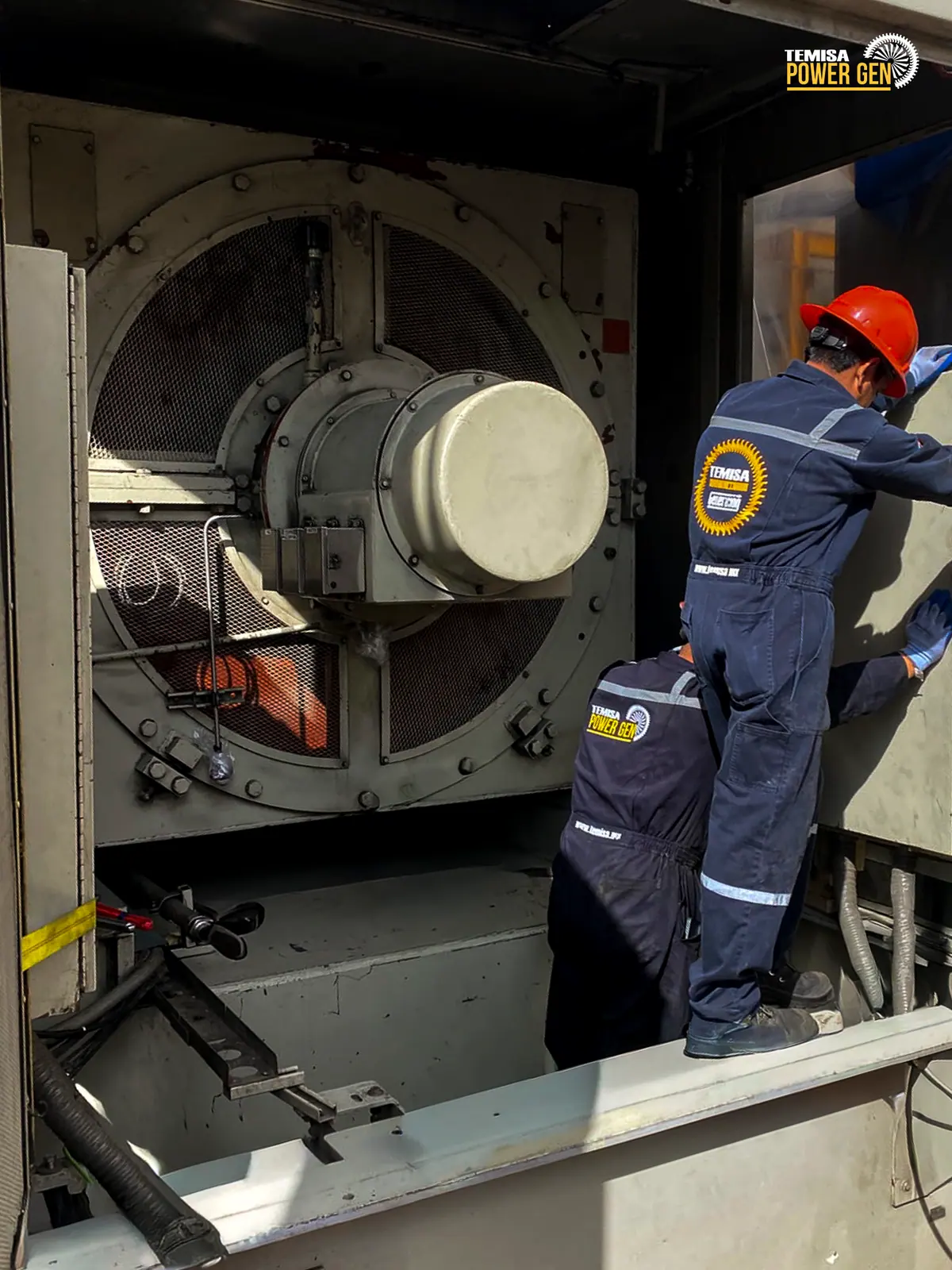 Technicians working beside the generator inside the enclosure.